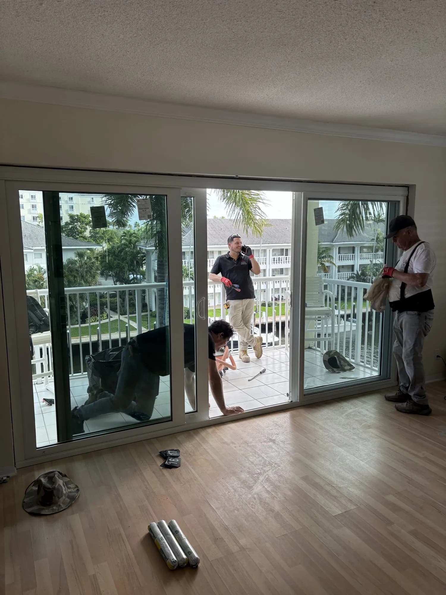Three installers finishing a white three-panel sliding glass door on a condo balcony