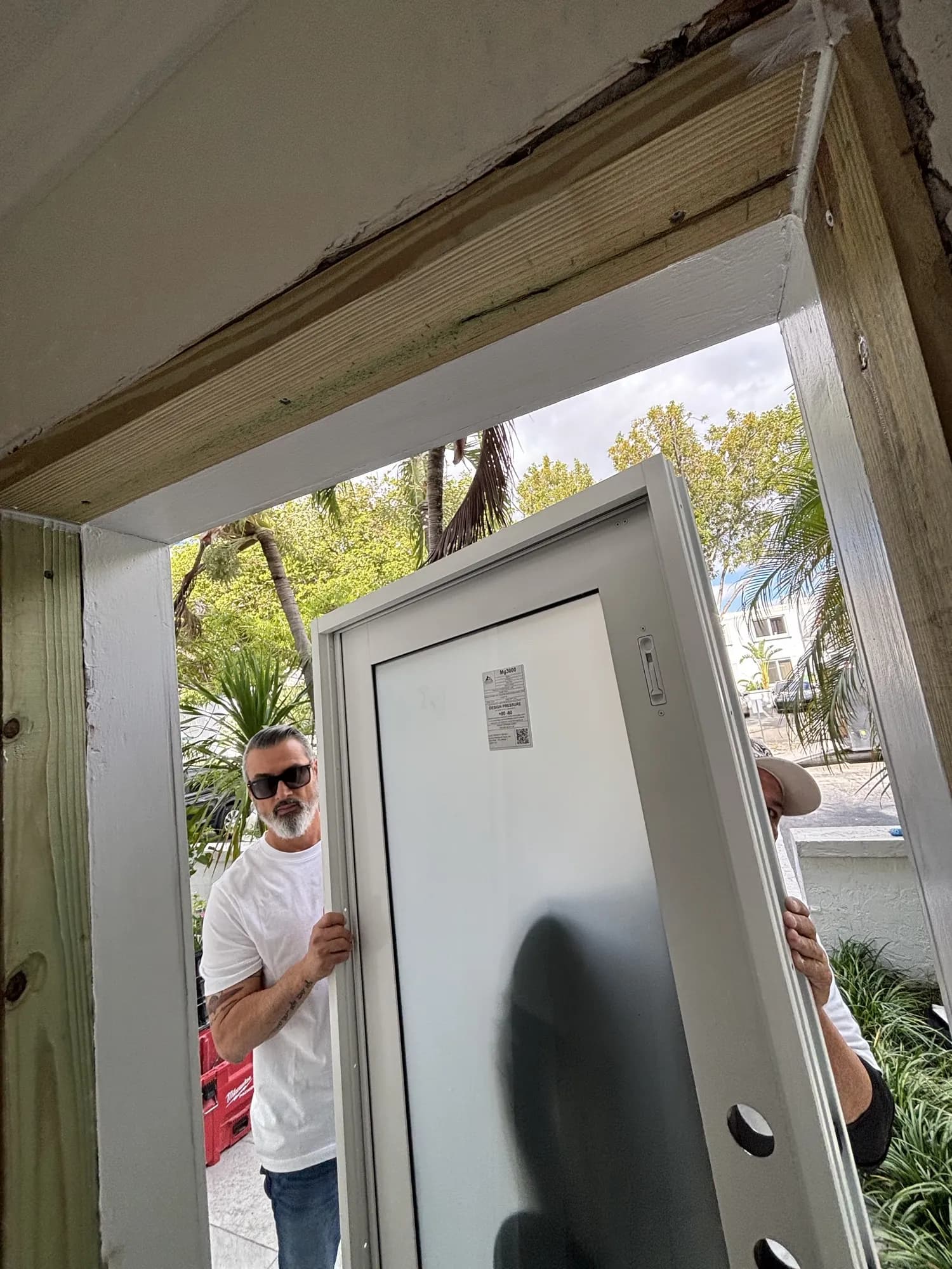 Atlantic Door Systems installers setting a white impact entry door into the frame on a South Florida job