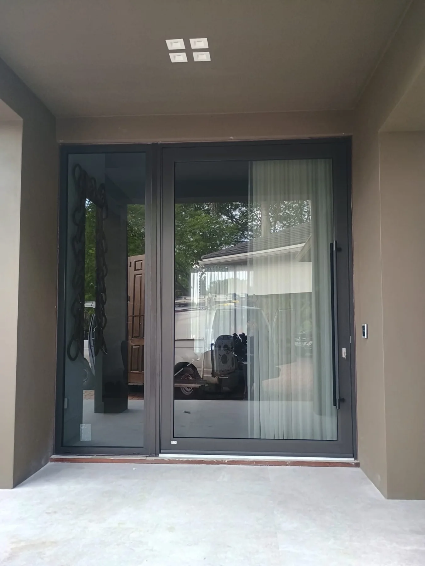 Black-framed glass impact pivot door with matching sidelight and vertical pull handle installed on a South Florida home
