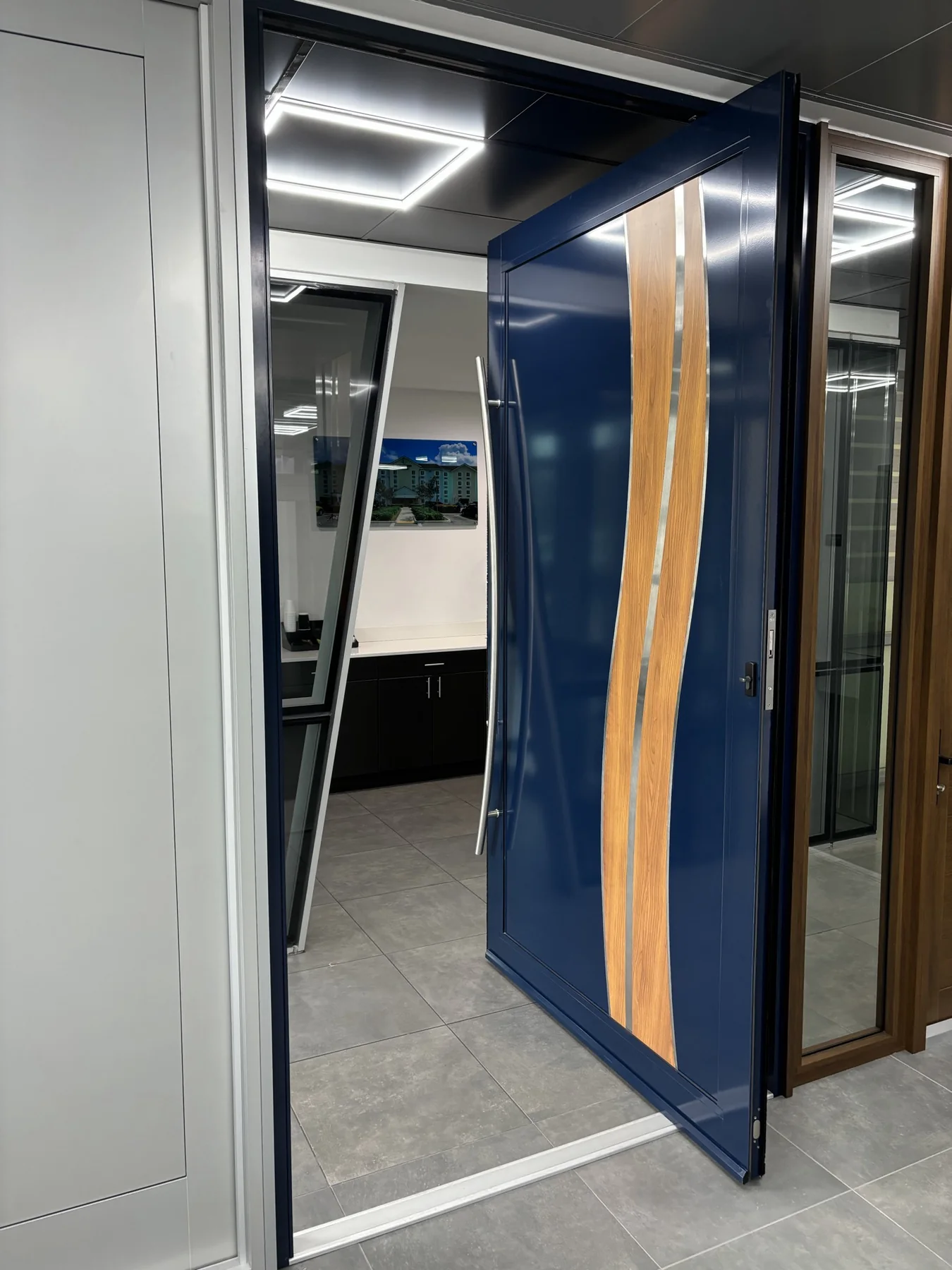 Glossy navy blue impact pivot door with curved wood-grain inlays and brushed metal pull handle in a Miami showroom