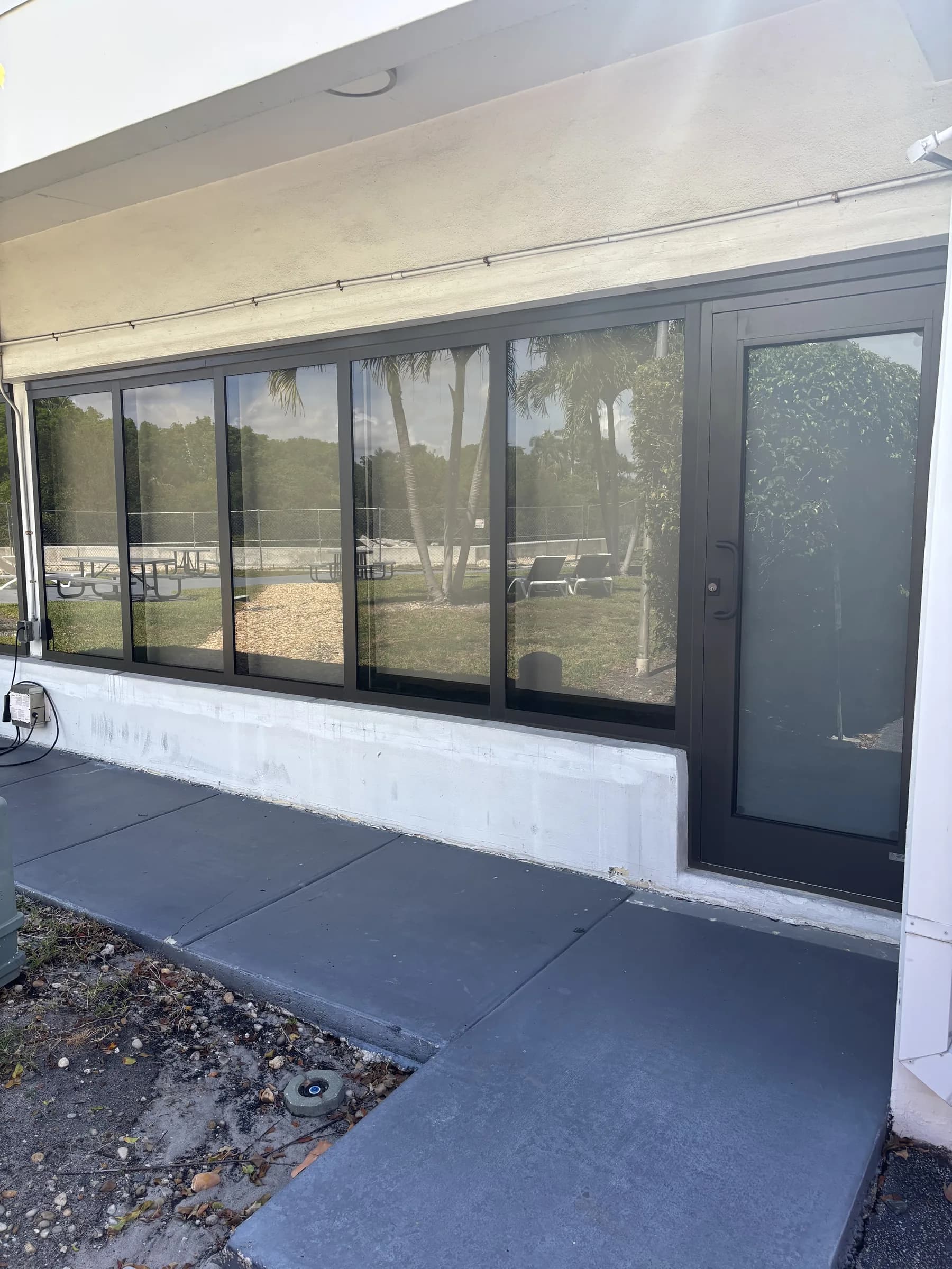 Dark-framed commercial impact door beside multipane storefront windows on a stucco building