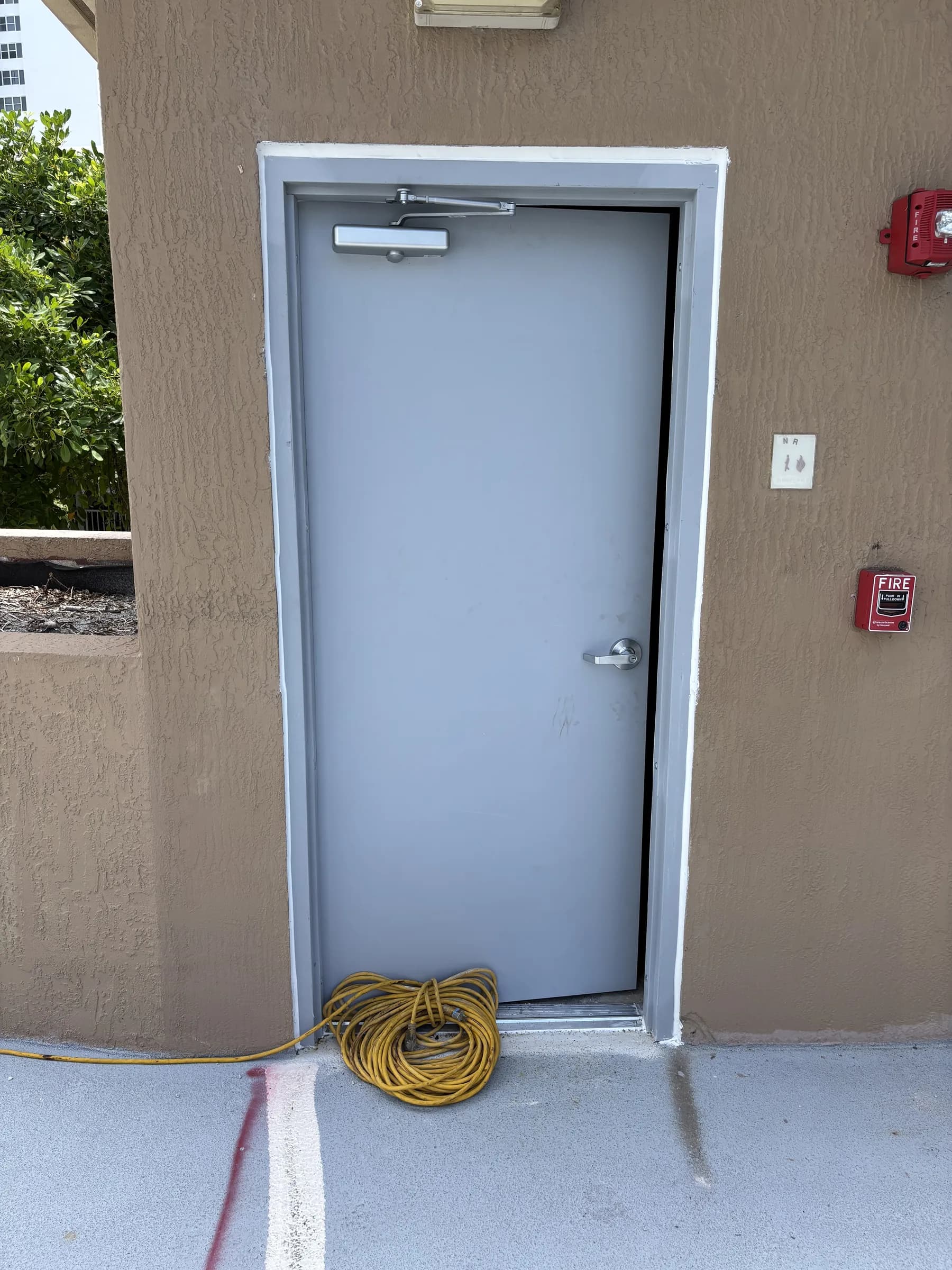 Exterior gray fire-rated commercial exit door with closer and fire alarm devices above