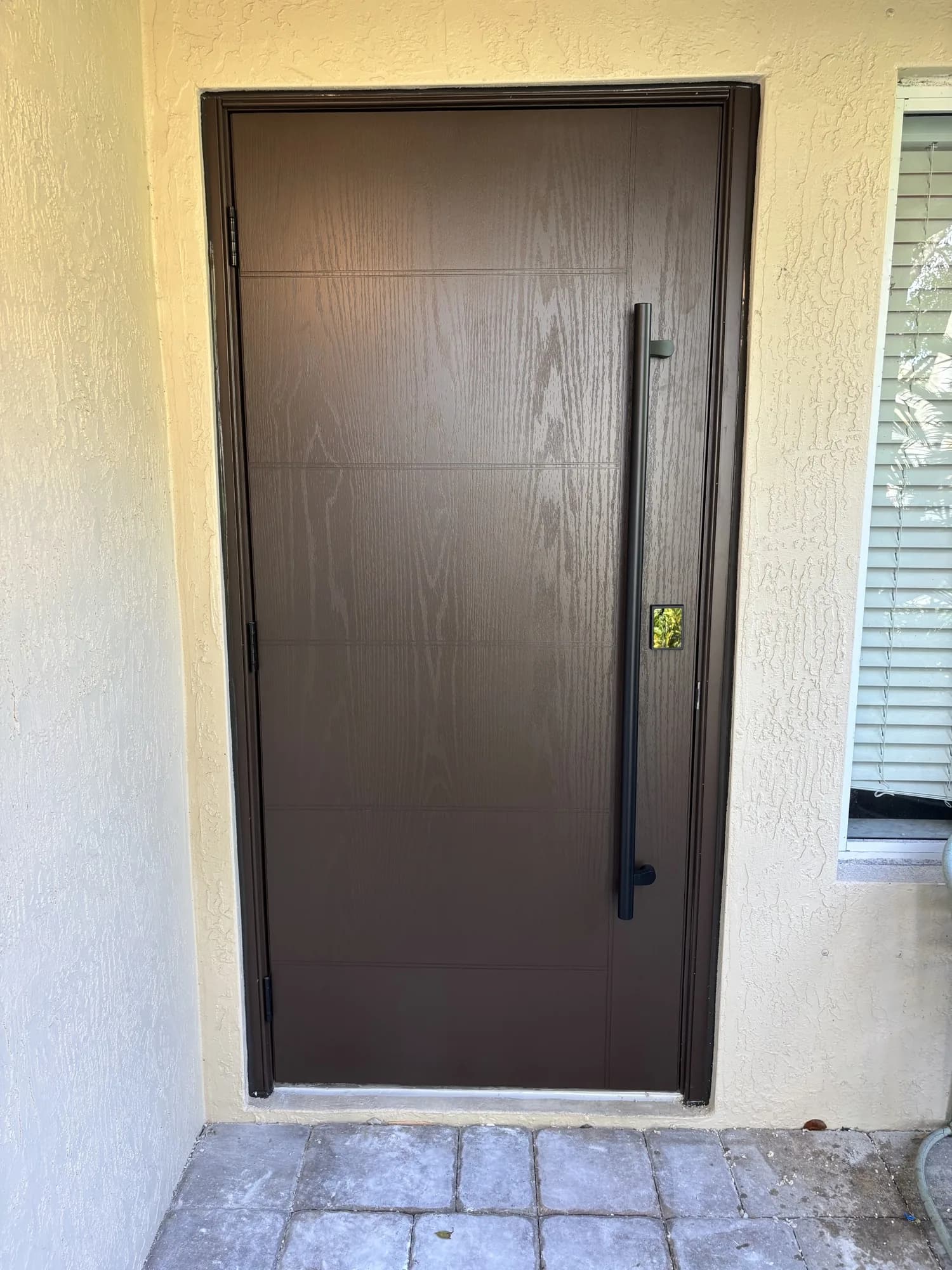 Dark wood-grain multifamily entry door with matte black vertical pull handle and smart lock