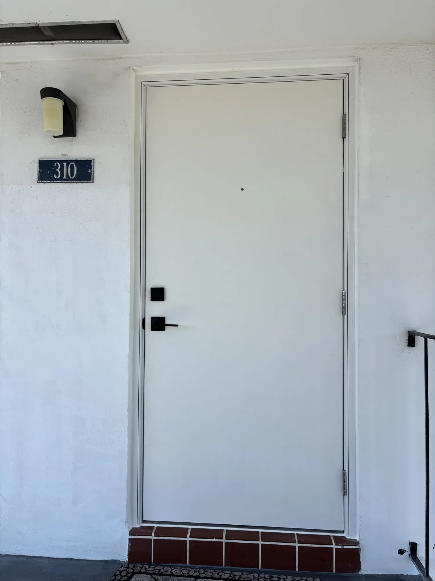 White flat-panel multifamily unit entry door with black lever hardware and unit number plaque