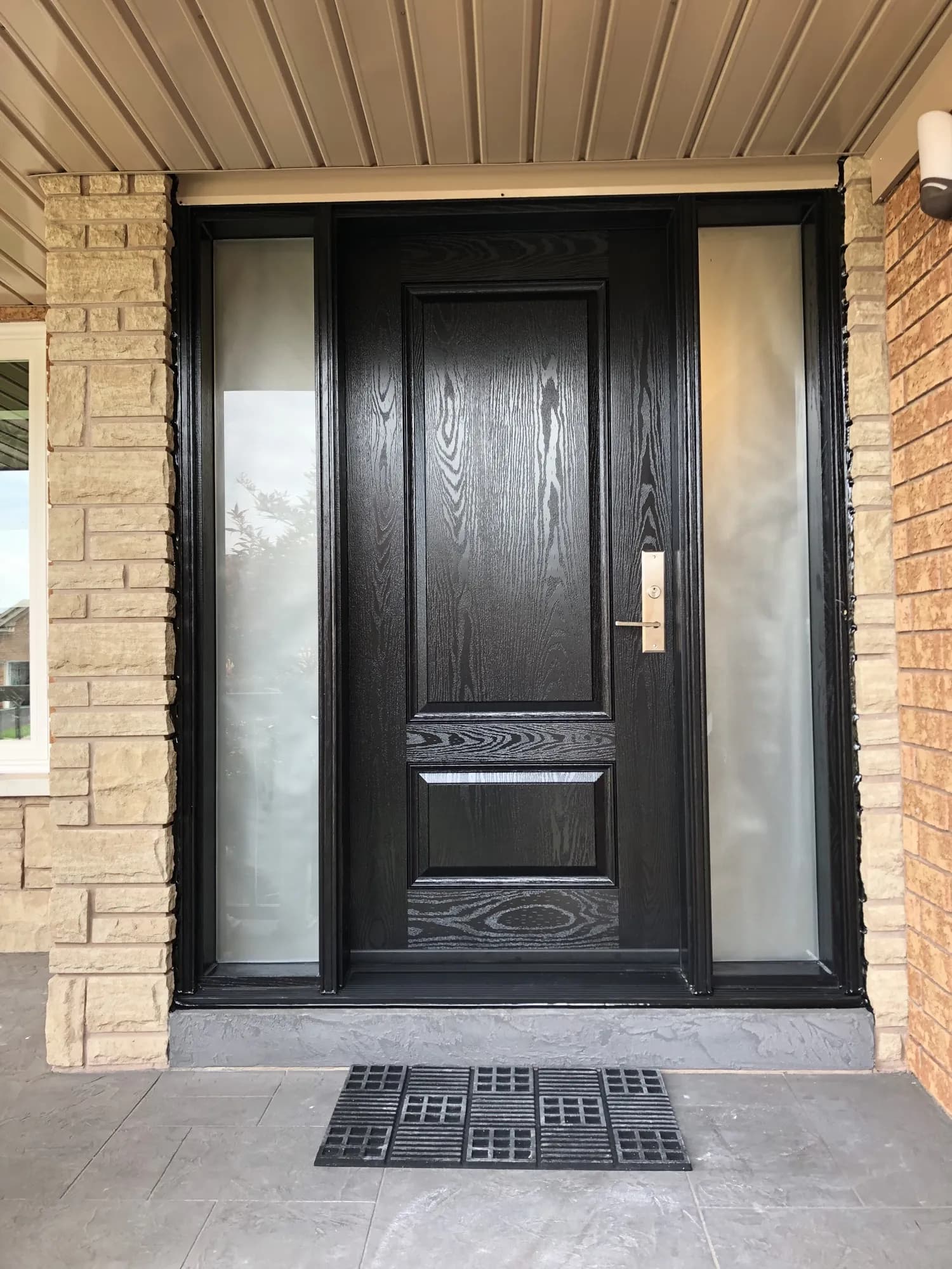 Black wood-grain entry door with frosted sidelights in a brick and stone porch