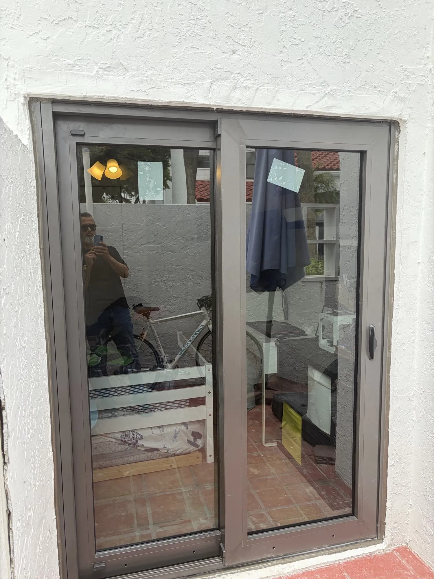 Dark bronze sliding glass door on a white stucco wall above terracotta tile