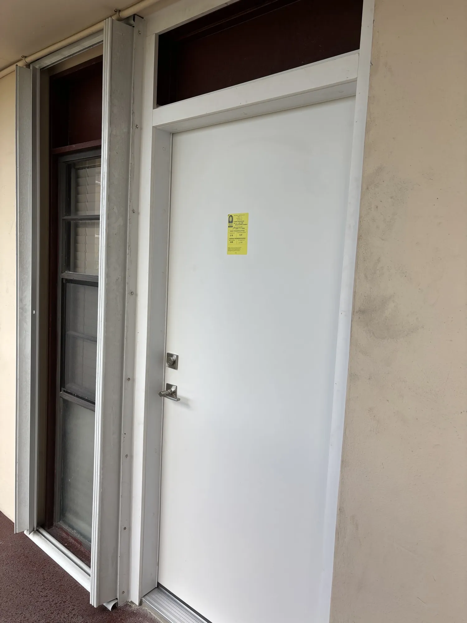 White entry door with permit sticker installed beside a narrow window with shutter tracks