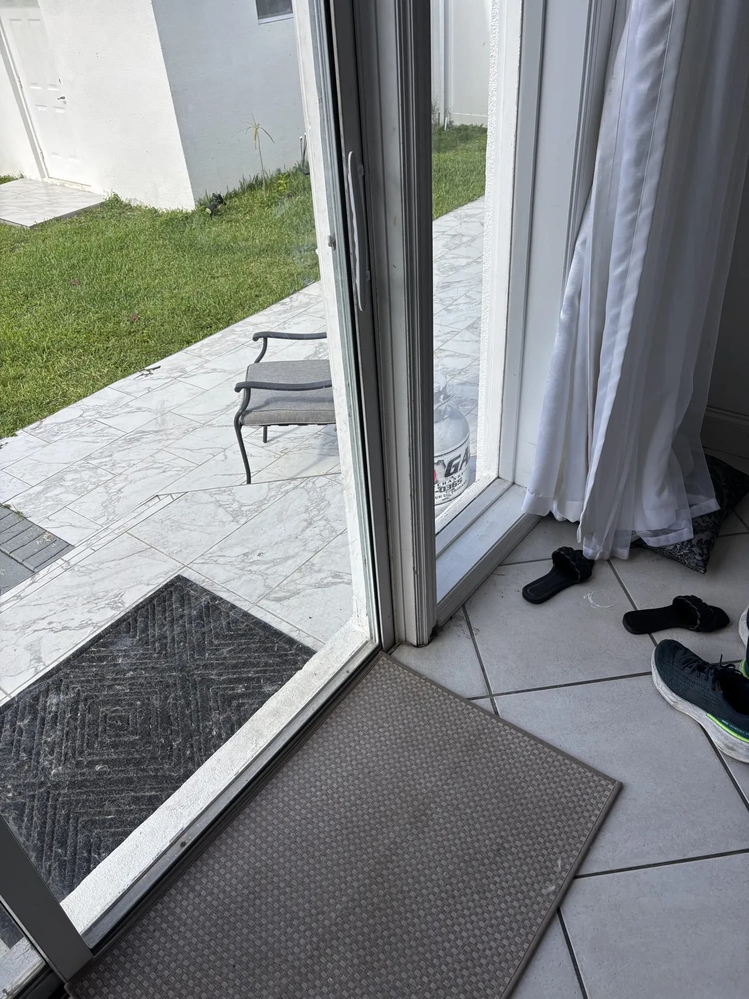 White sliding glass door open to a tiled patio and backyard