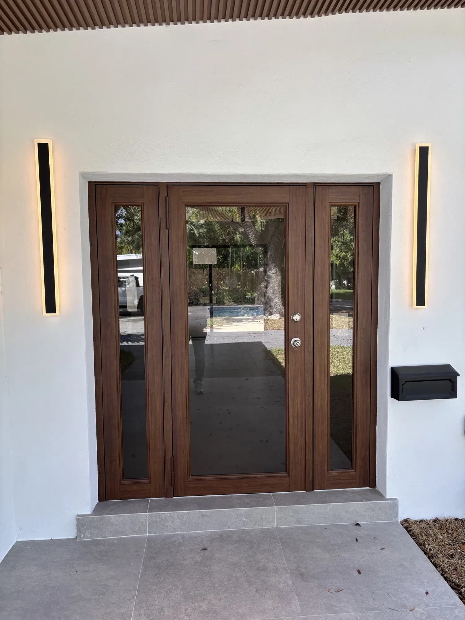 Wood-grain entry door with matching glass sidelights and vertical exterior lighting