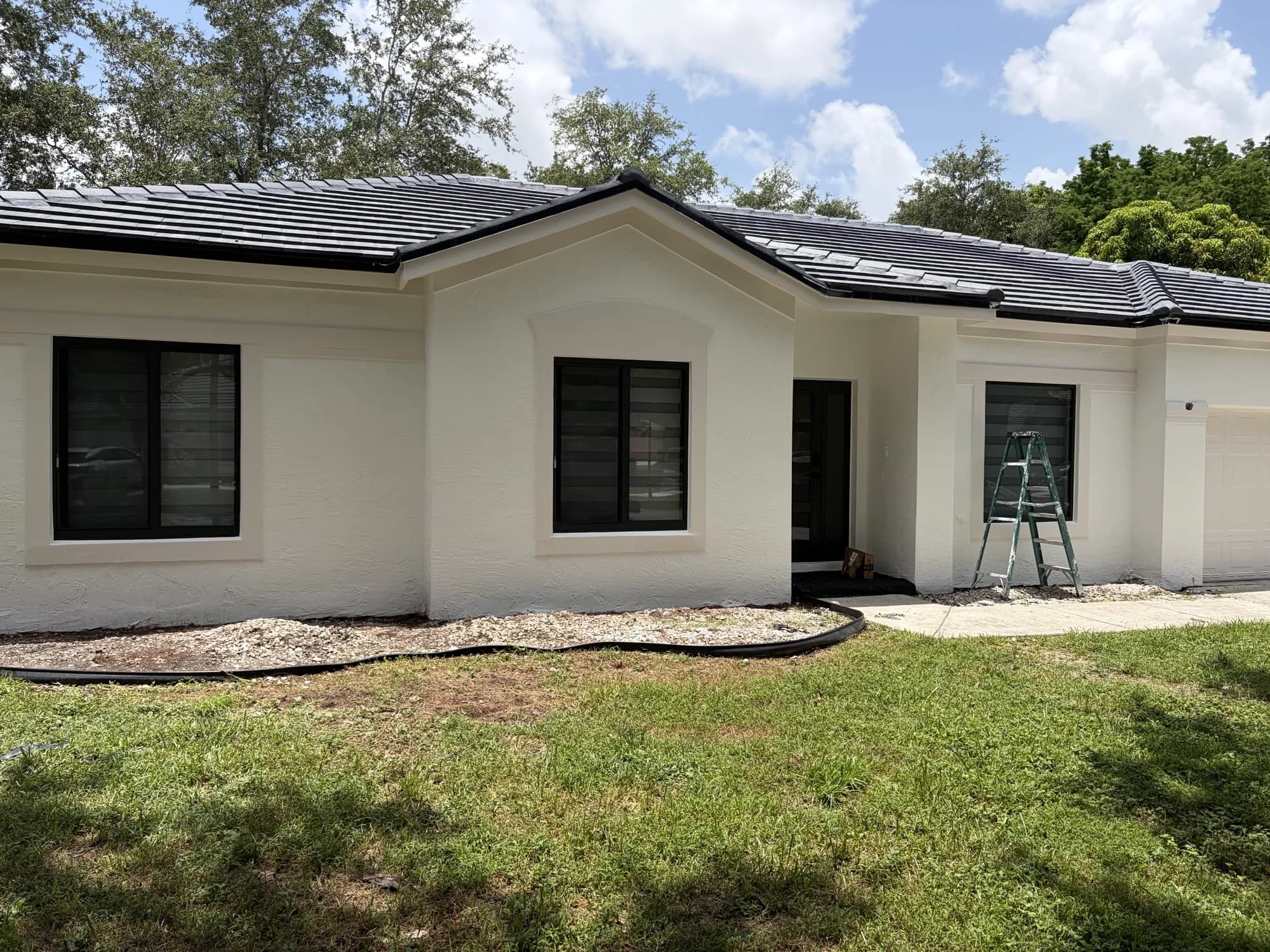 Front of a stucco home with three new black-framed windows during installation