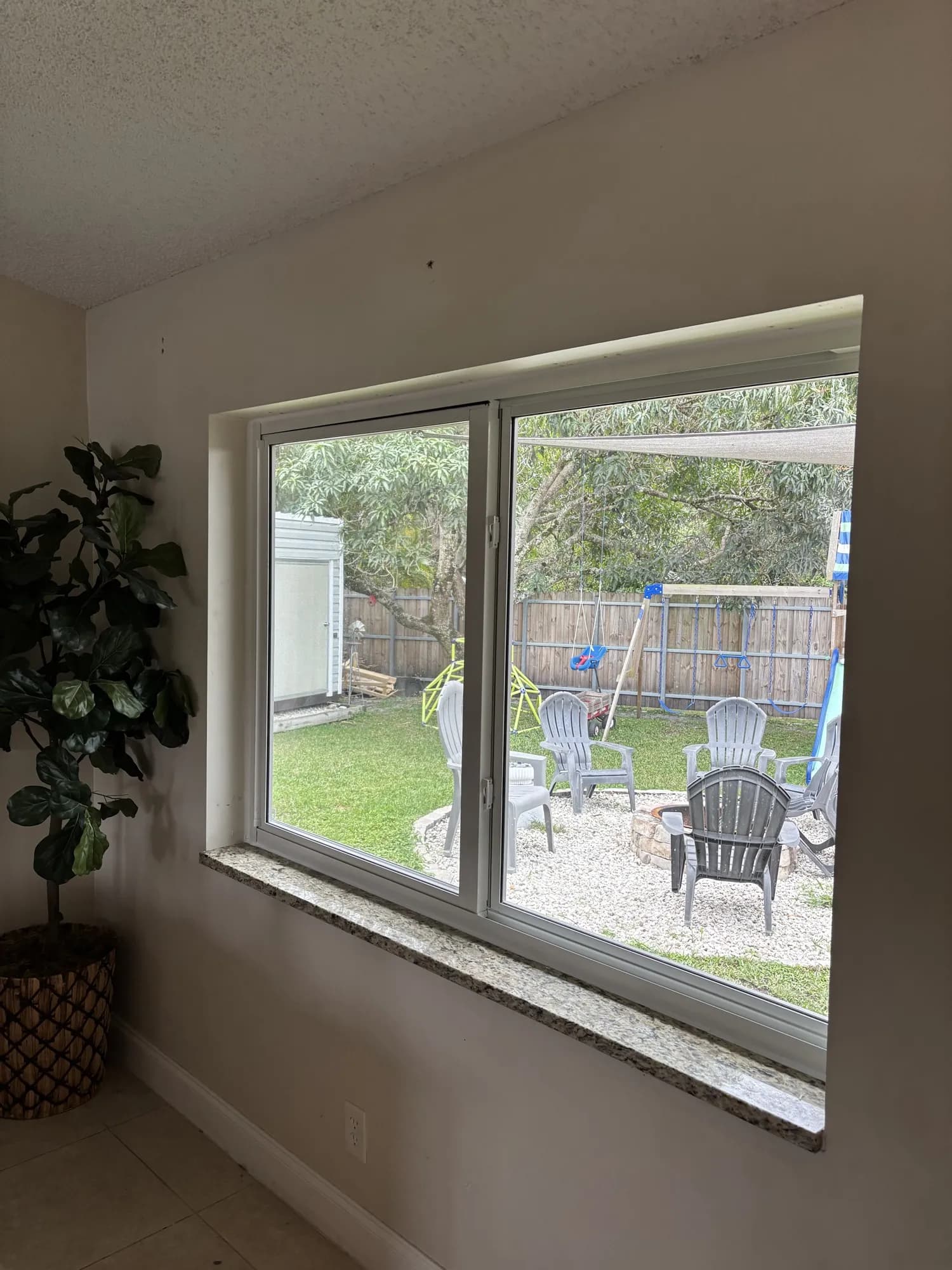 Interior white-framed window overlooking a backyard with lawn and fire pit