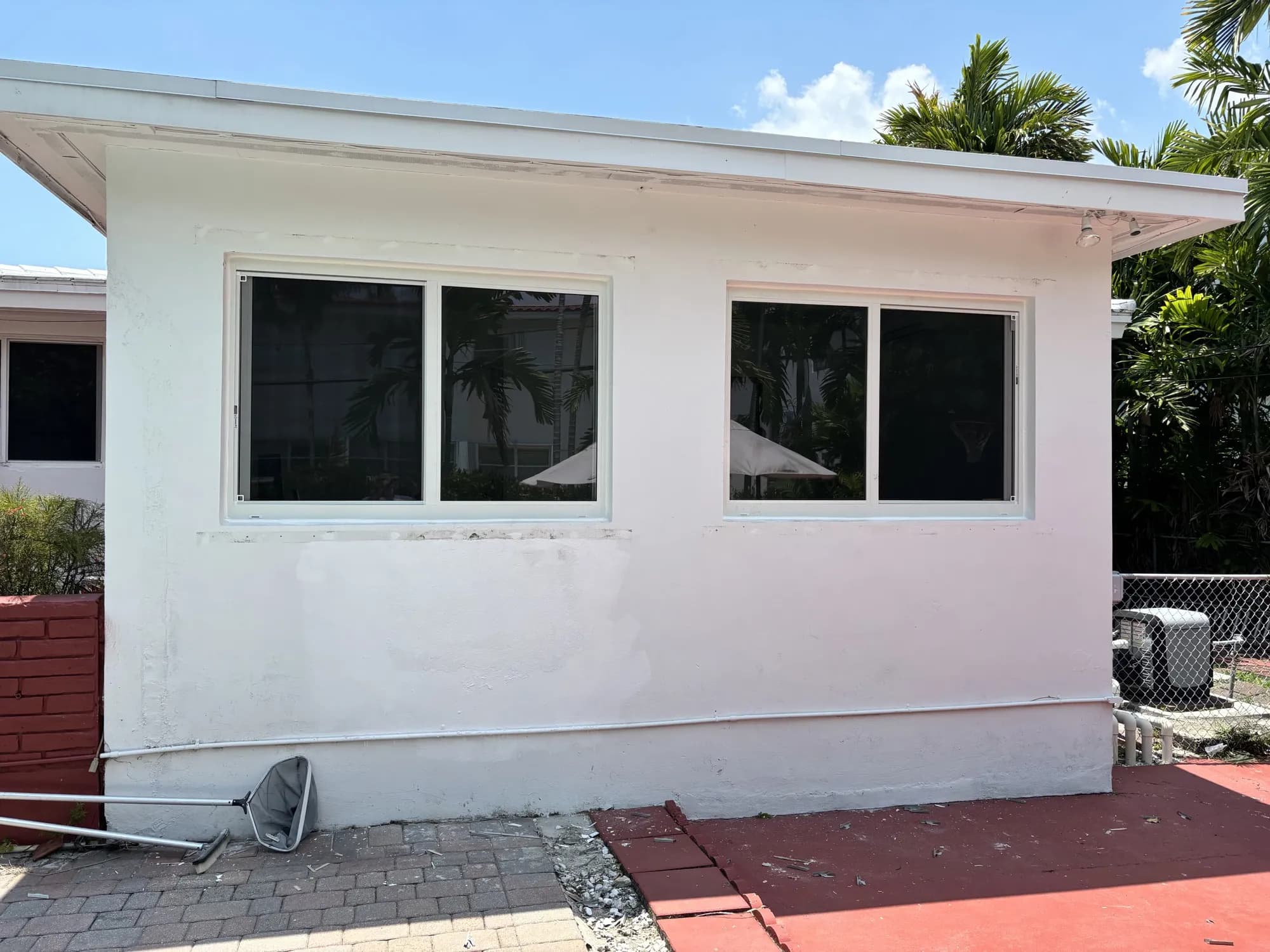 Two white horizontal sliding windows installed in a stucco wall beside a pool patio