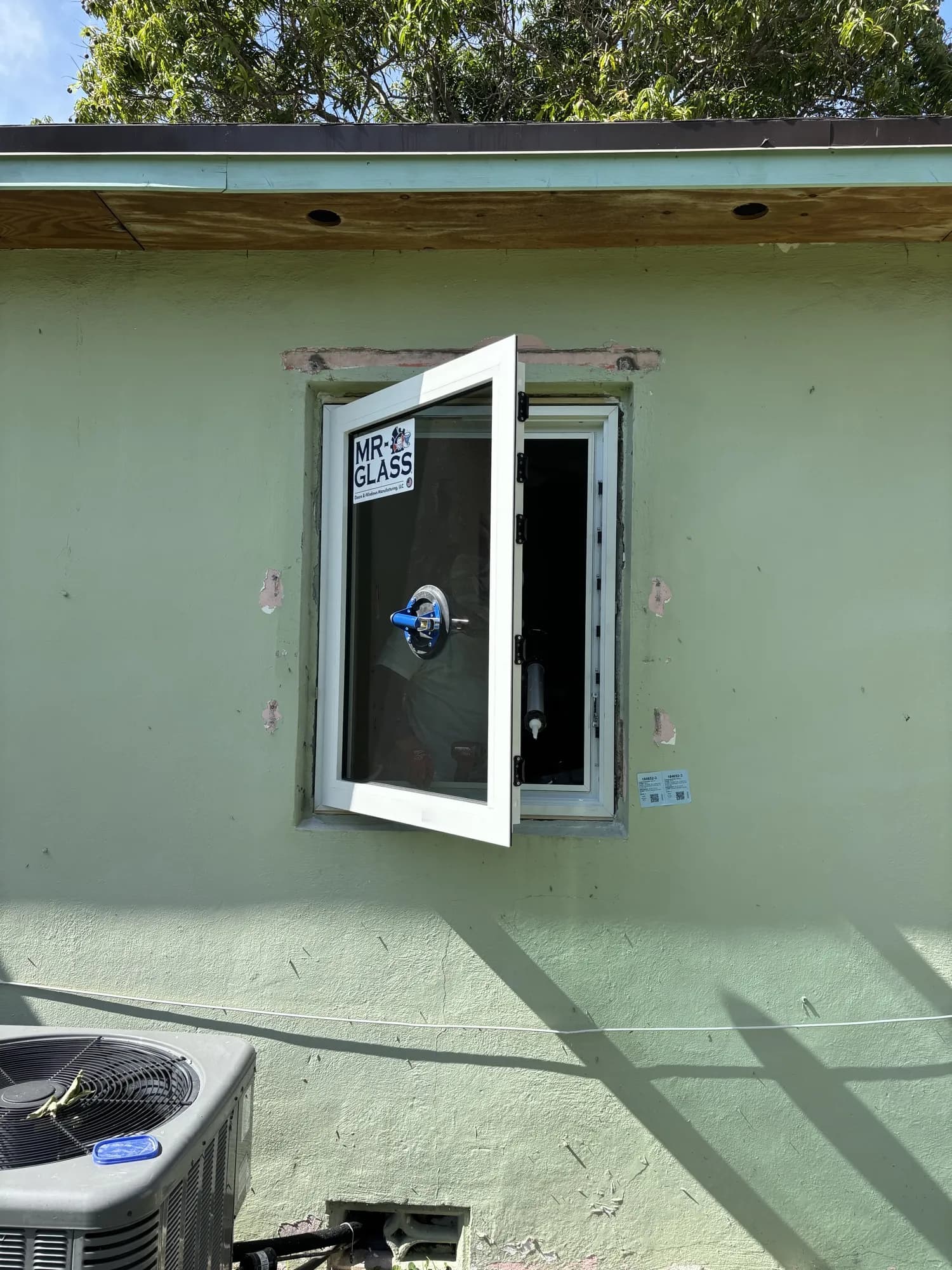 White casement window open during installation on a green stucco wall