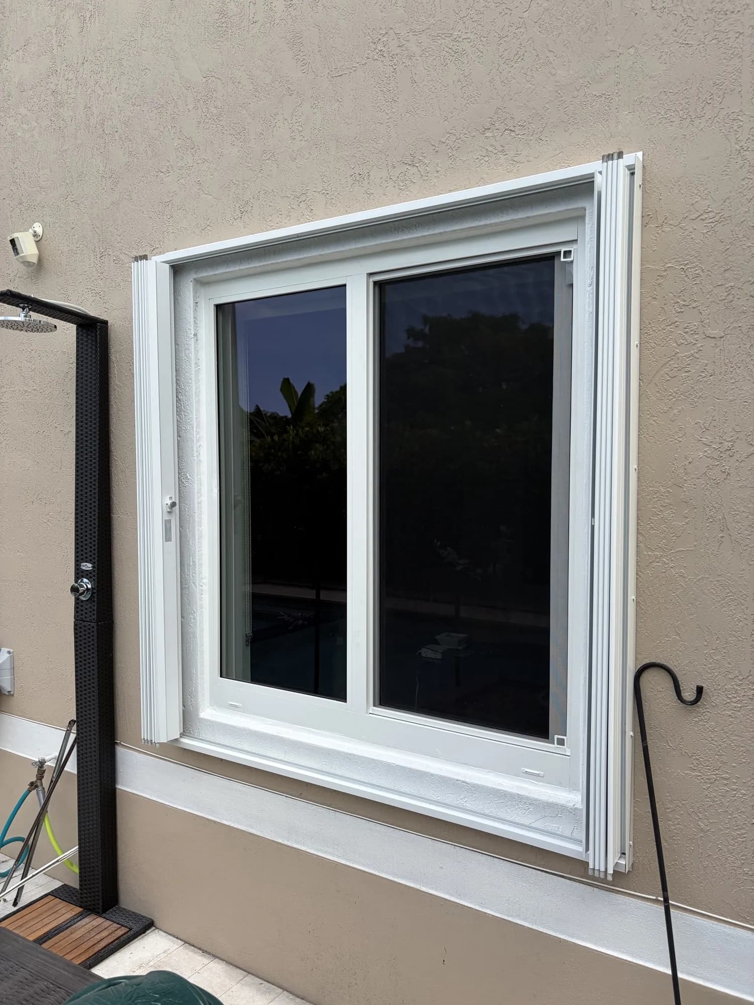 White horizontal sliding window with accordion hurricane shutters on a stucco patio wall