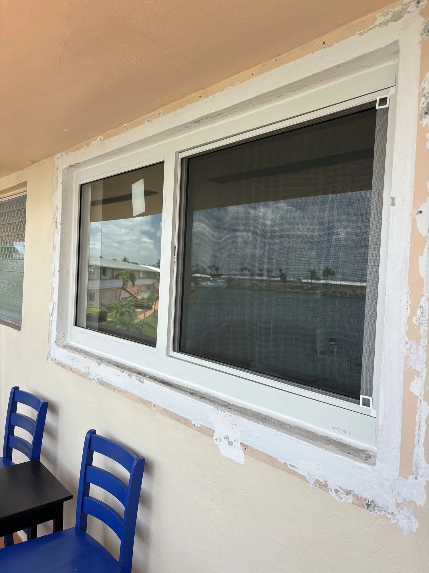 White horizontal sliding window with fresh stucco patch on a balcony wall